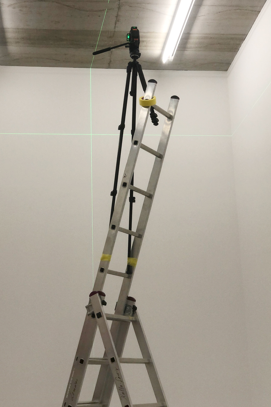 A letter with a cross-line laser taped to the final steps, the cross-line laser is projecting a green cross on the adjacent white wall.