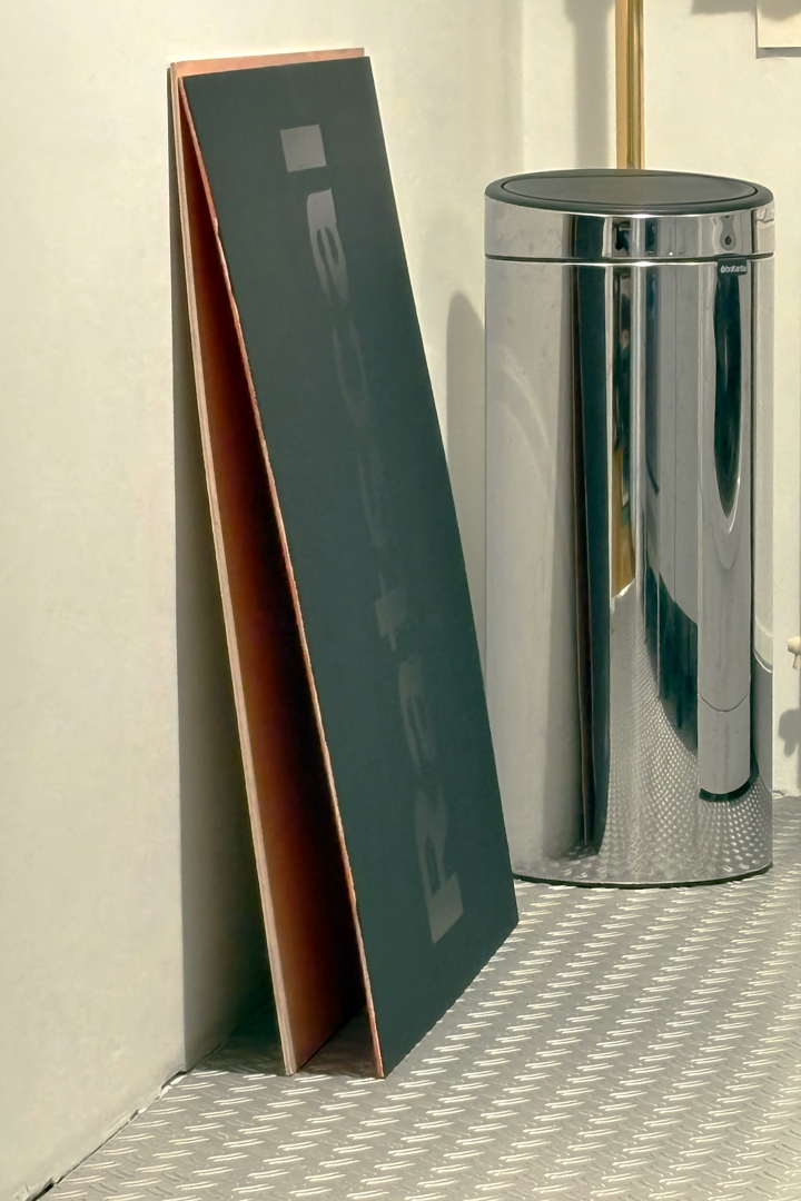 A black painting leaning up against a white wall, next to it is a chrome transcan.